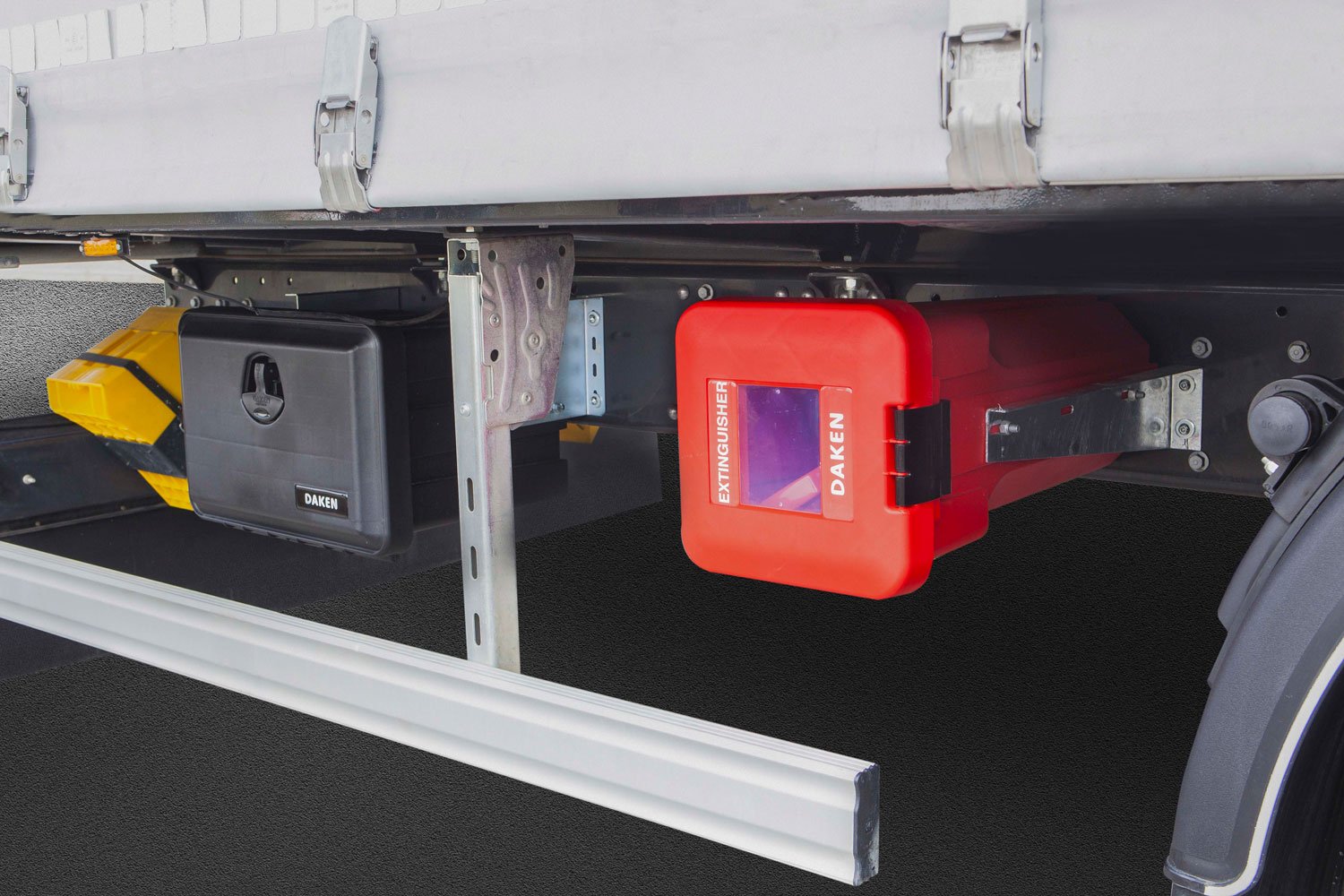 Daken Sliden | Porta estintore in plastica rosso con vetro d'ispezione, installato sotto a un camion in orizzontale, con accanto una cassetta porta attrezzi in plastica Daken