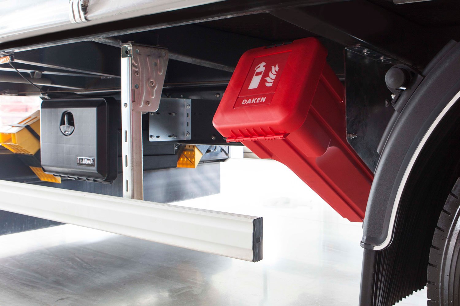 Daken Sliden | Porta estintore in plastica rosso con vetro d'ispezione, installato su camion in obliquo, con accanto una cassetta porta attrezzi in plastica Daken